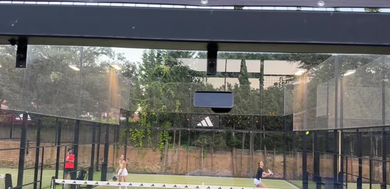 An iPhone on a suction mount on the back glass of a padel court, filming the game